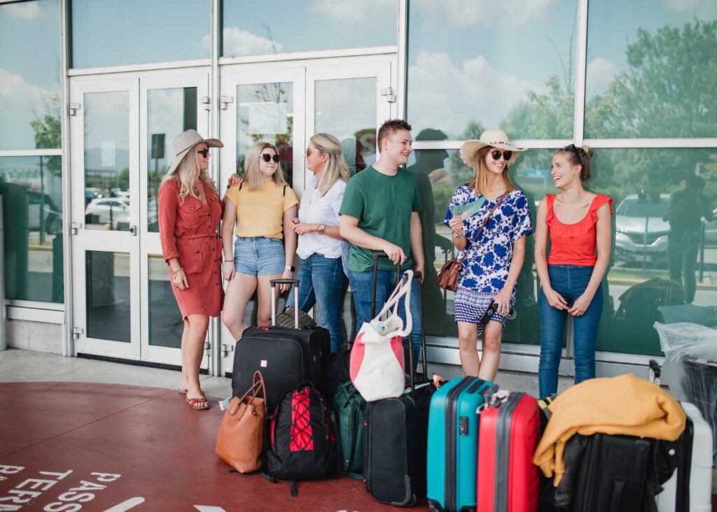 A group of individuals with luggage stands in front of a building, ready for travel or awaiting transportation.