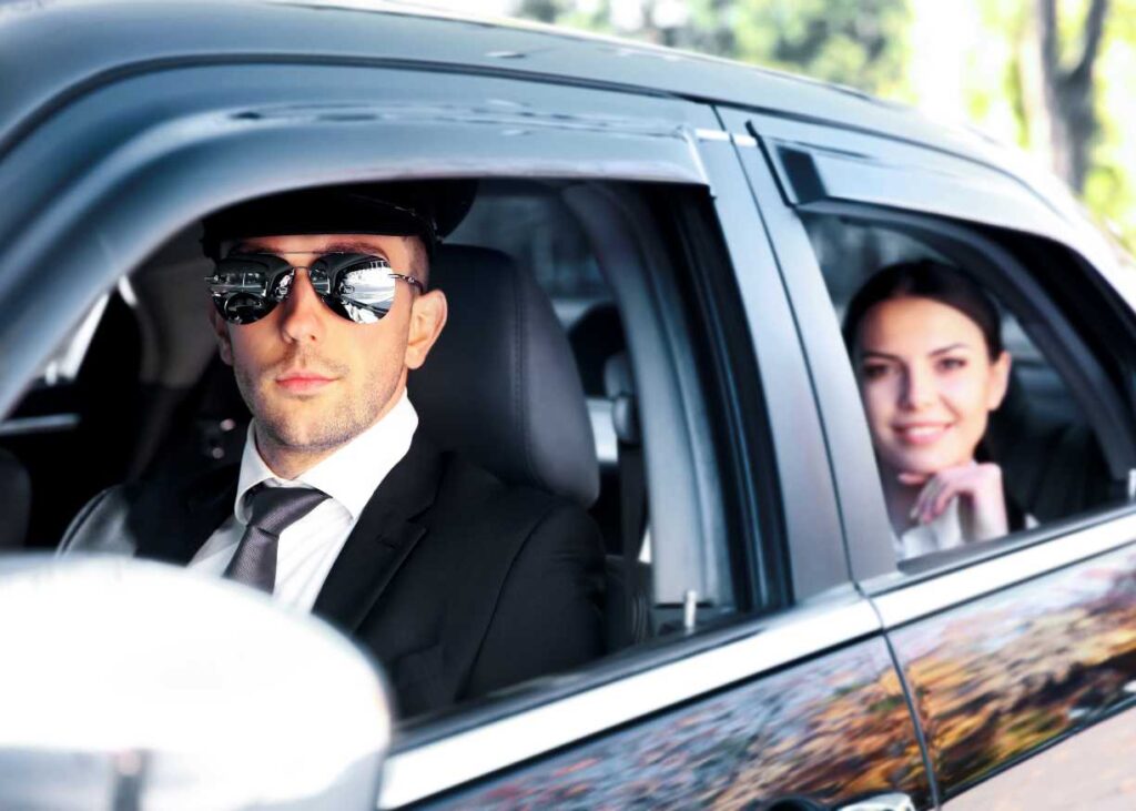 A man and woman wearing sunglasses sit together in a car, enjoying their time on a sunny day.