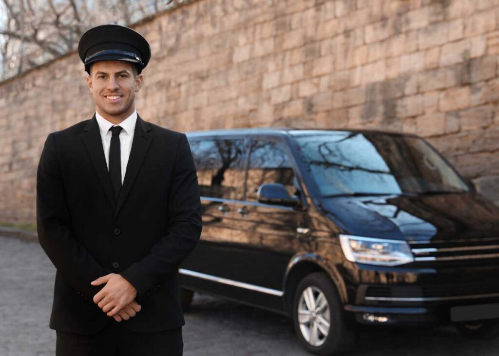 A man in a suit and tie stands beside a sleek black van, exuding professionalism and confidence.