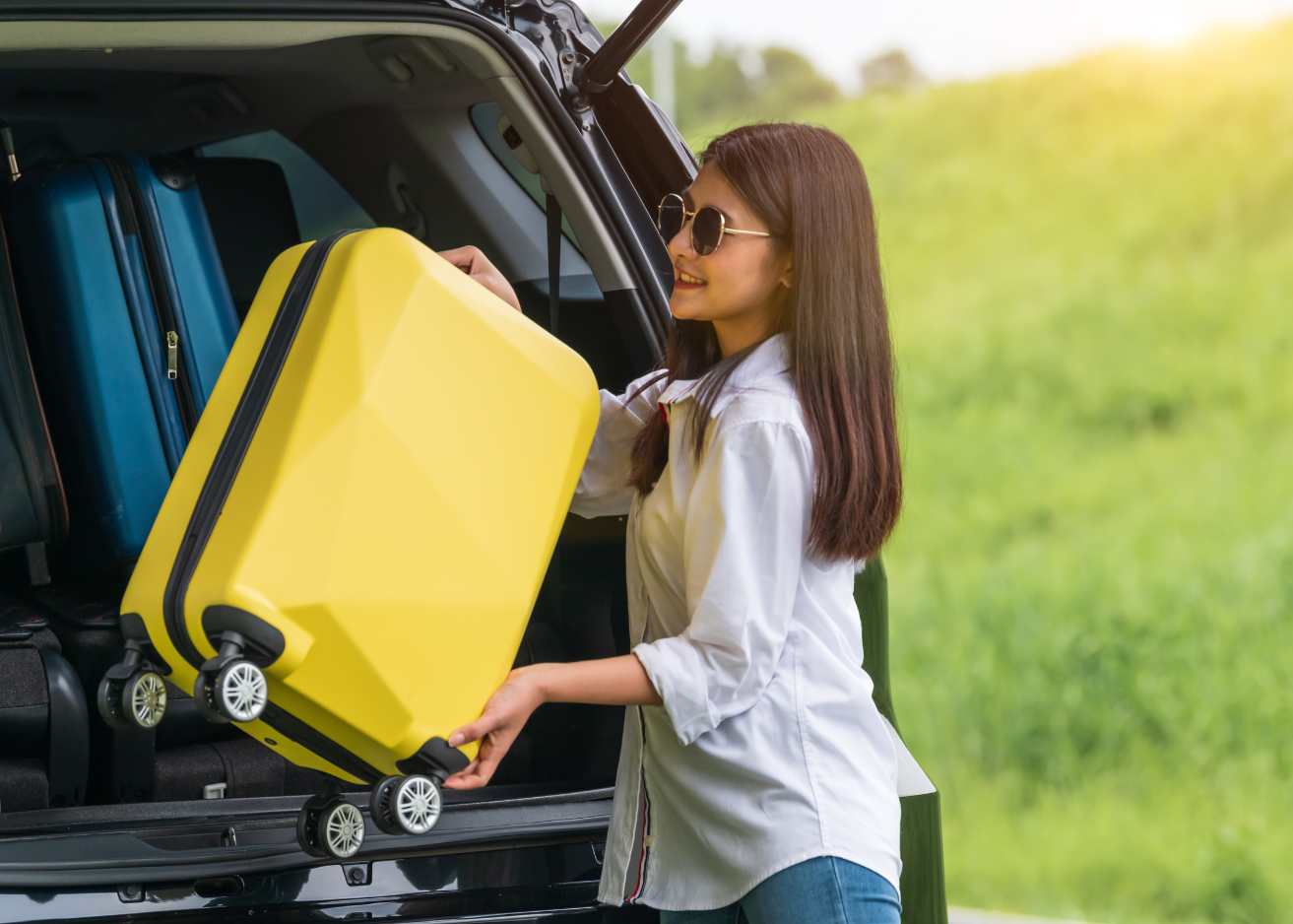 Asian woman placing a yellow suitcase into the trunk of a car, preparing for travel or a journey.