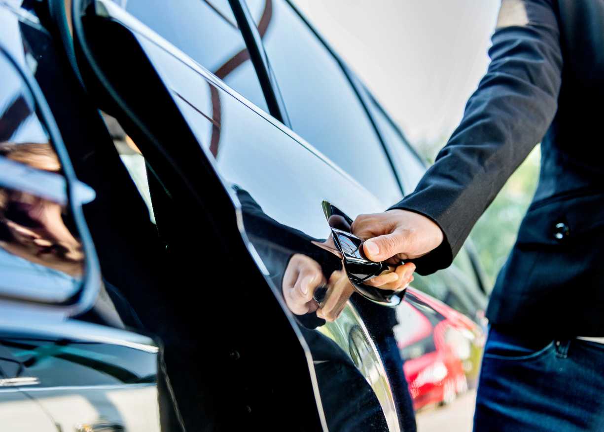 A person gripping the door handle of a sleek black car, ready to enter or exit the vehicle.