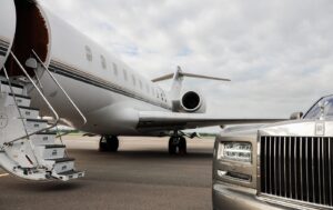 A silver Rolls Royce parked beside a private jet, showcasing luxury and elegance in a lavish setting.