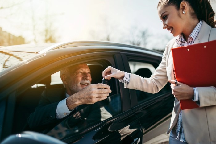 A woman is handing a car key to a man, symbolizing a transfer of responsibility or ownership.