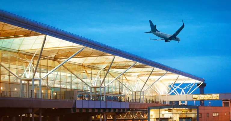 An airplane soars above an airport terminal, showcasing the dynamic activity of air travel.