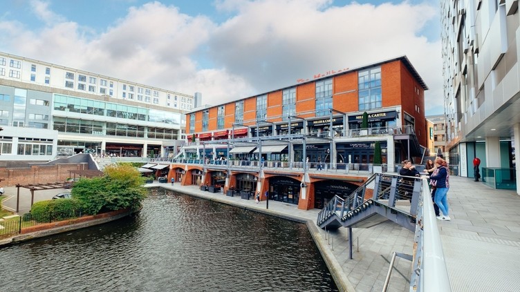 A scenic canal with a building in the background, featuring pedestrians strolling along the water's edge.