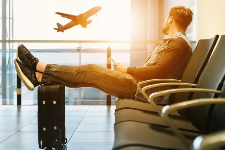 A man sits cross-legged on a chair, with a suitcase placed in front of him.