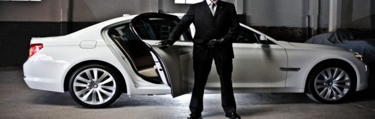 A man in a suit stands beside a sleek white car, exuding professionalism and elegance.