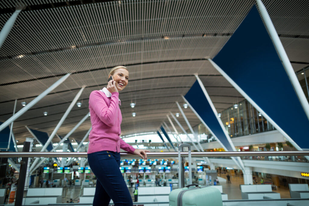 Female commuter with luggage talking on mobile phone in airport