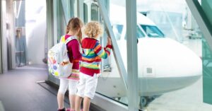 Two children gazing out of an airport terminal, captivated by an airplane on the tarmac.