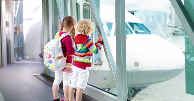 Two children gazing out of an airport terminal, captivated by an airplane on the tarmac.