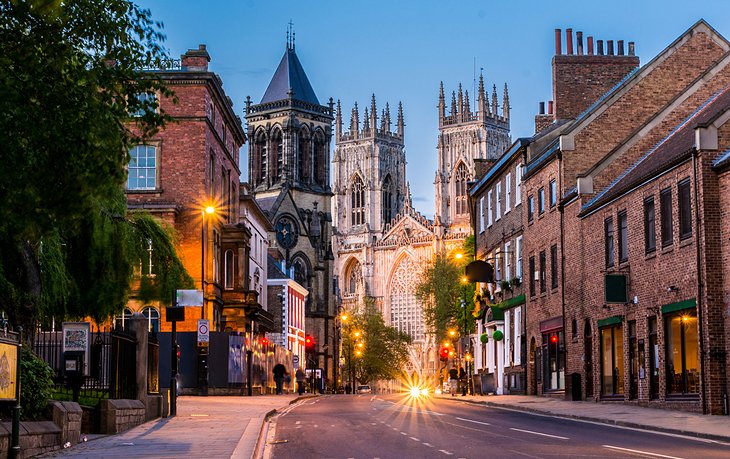 A street scene featuring a majestic cathedral rising in the background, framed by buildings and trees.