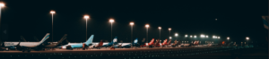 A row of airplanes parked under the night sky, illuminated by airport lights, creating a serene and tranquil atmosphere.