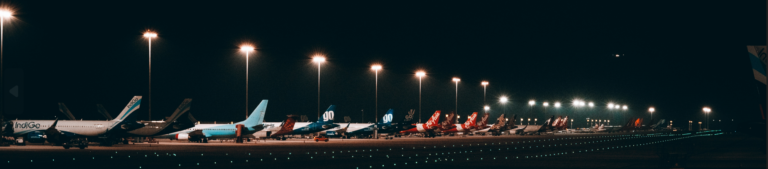 A row of airplanes parked under the night sky, illuminated by airport lights, creating a serene and tranquil atmosphere.