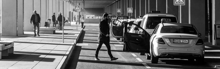 A black and white image depicting several cars parked in a spacious parking lot.