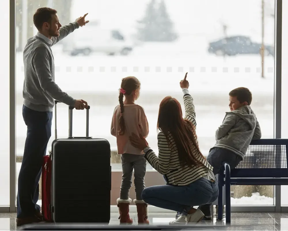 A family stands by a window, surrounded by luggage, ready for their journey together.