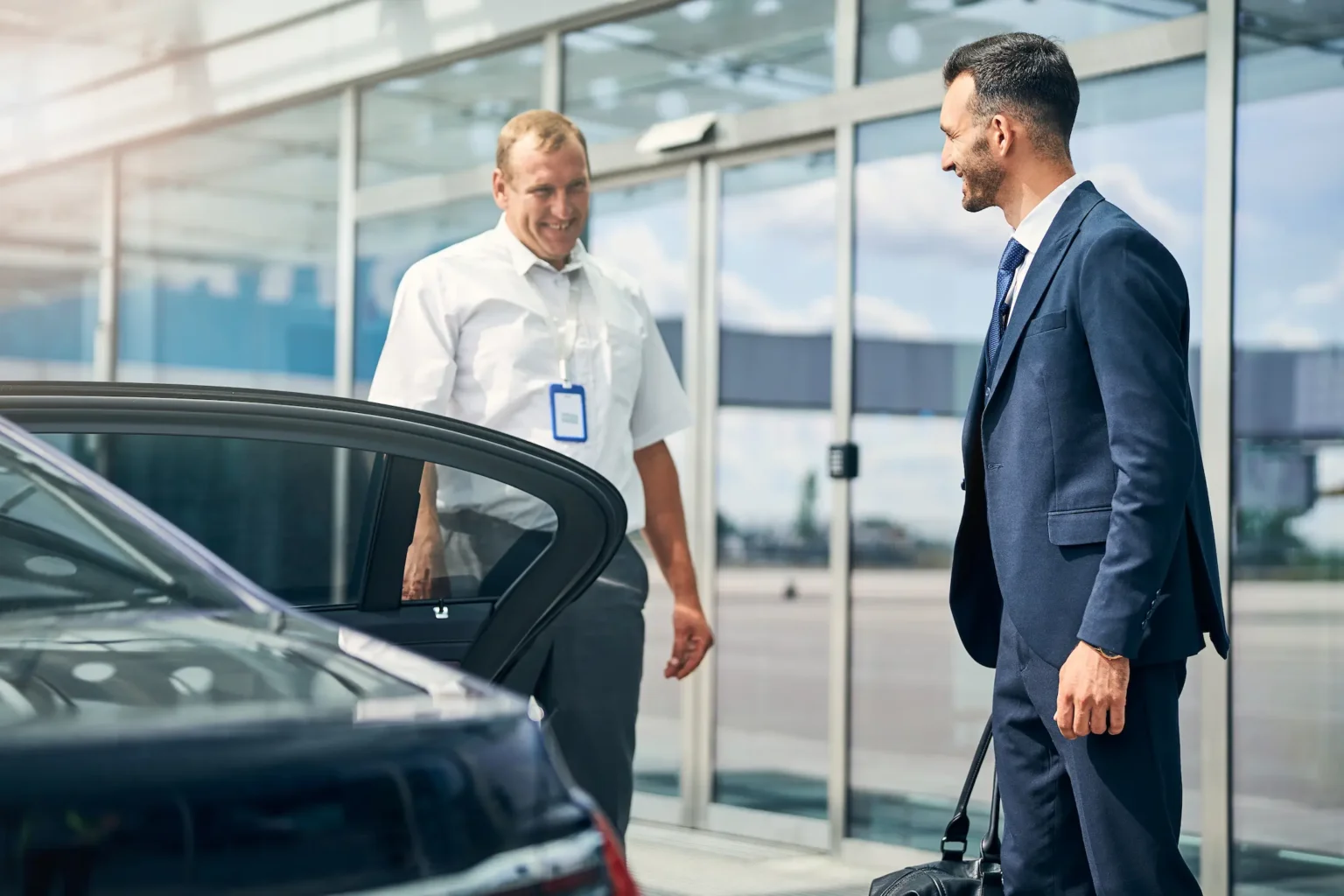 Two men in suits standing beside a luxury car, exuding professionalism and confidence in a formal setting.