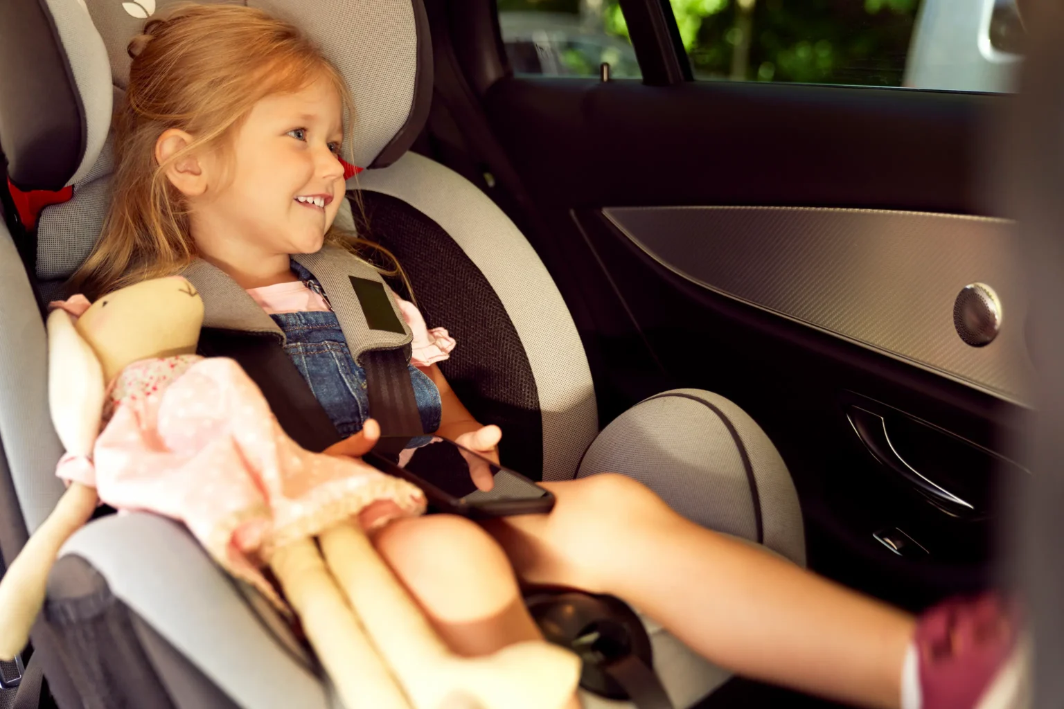 A young girl in a car seat cuddles a stuffed animal, showcasing a moment of comfort and innocence.