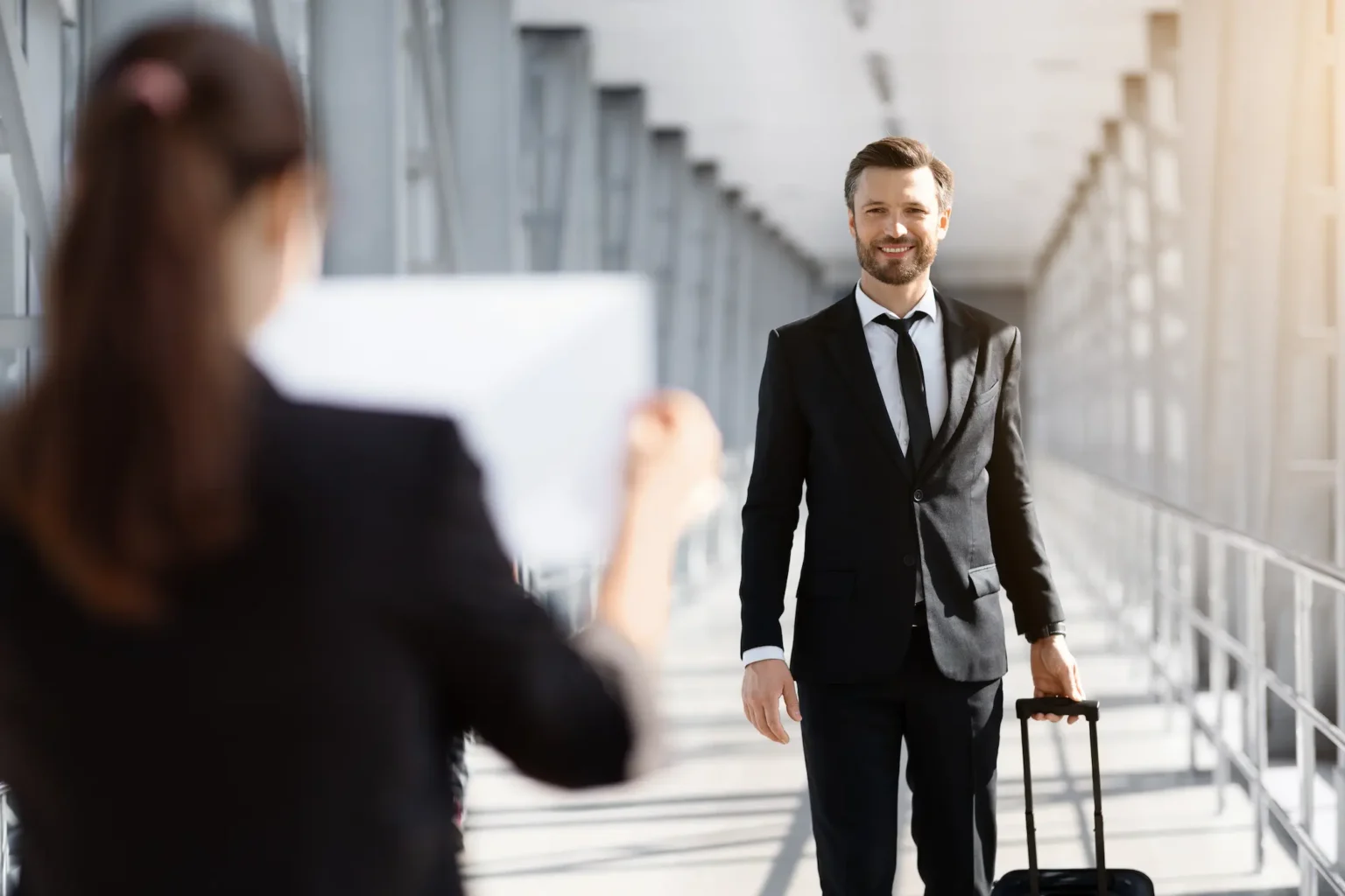 A businessman in a suit and tie walks confidently with his luggage in a professional setting.