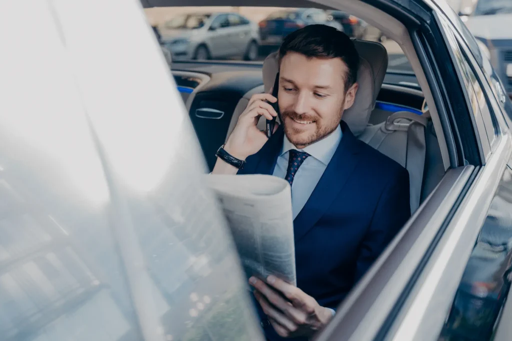 A man in a suit and tie seated in a car's back seat, engaged in a phone conversation.