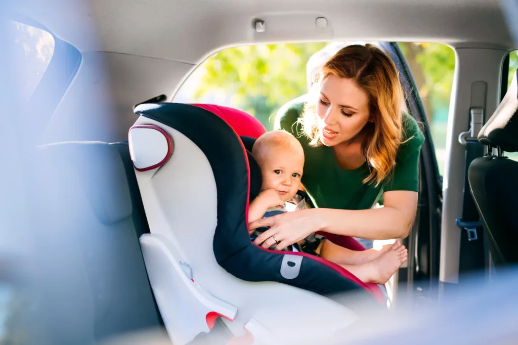 A woman assists a baby securely seated in a car seat, ensuring the child's safety and comfort during travel.