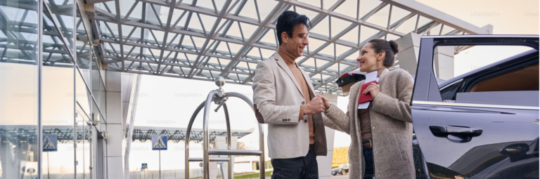 A man and woman stand together in front of a parked car, smiling and enjoying their time outdoors.