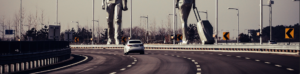 A car travels along a highway, passing a prominent statue of a man alongside the road.