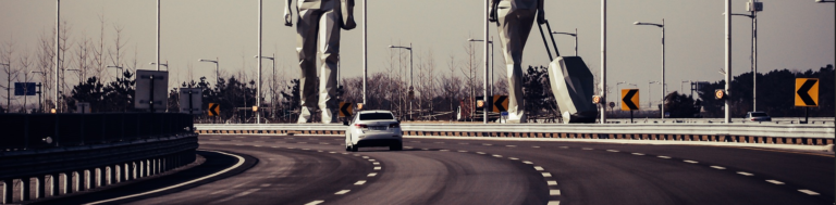 A car travels along a highway, passing a prominent statue of a man alongside the road.