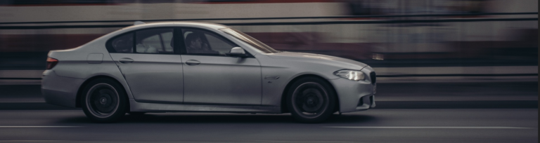 A silver car travels along a road, showcasing its sleek design against the backdrop of the landscape.