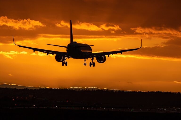 A large airplane soars through a vibrant sunset sky, casting a silhouette against the colorful horizon.