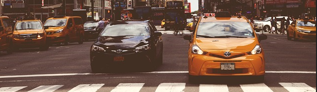 A yellow taxi cab drives along a city street, showcasing urban life and transportation.