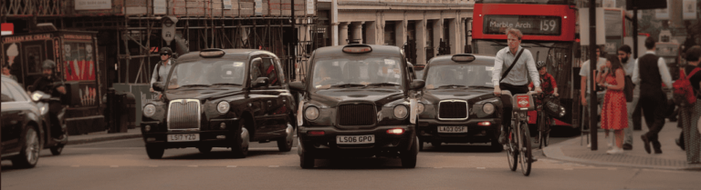 A fleet of black taxis navigating through a bustling city street.