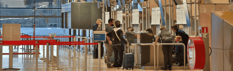 A queue of travelers waiting at an airport, with luggage in hand and signs indicating flight information nearby.