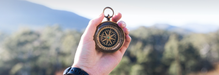 A person holds a compass in their hand, symbolizing navigation and exploration in the great outdoors.