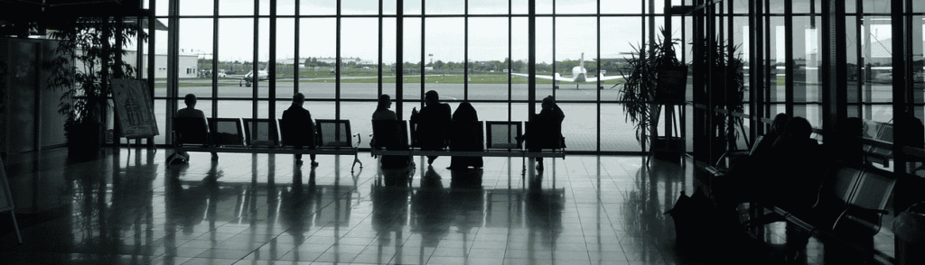 People walking through a bustling airport terminal, carrying luggage and navigating towards their gates.