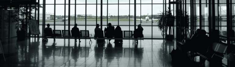 People walking through a bustling airport terminal, carrying luggage and navigating towards their gates.