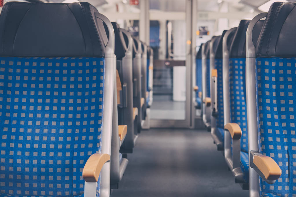 Rows of blue fabric seats with leather headrests on both sides of an aisle inside empty modern train, travel concept, selective focus.