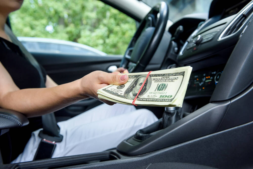 Bribe concept. Female hands giving dollar bundle inside car close