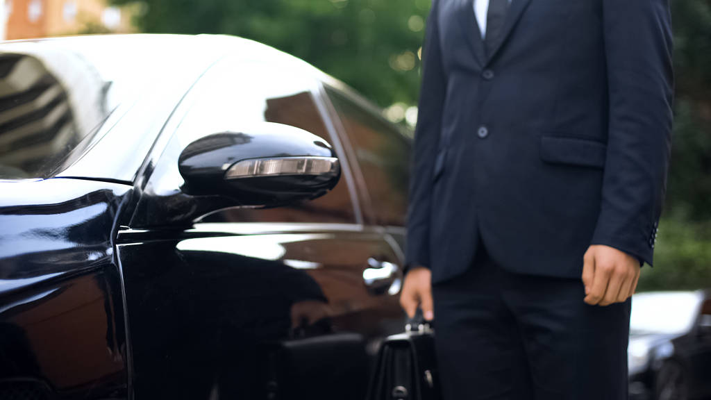 Premium class driver standing near luxury car, work for refugees,
