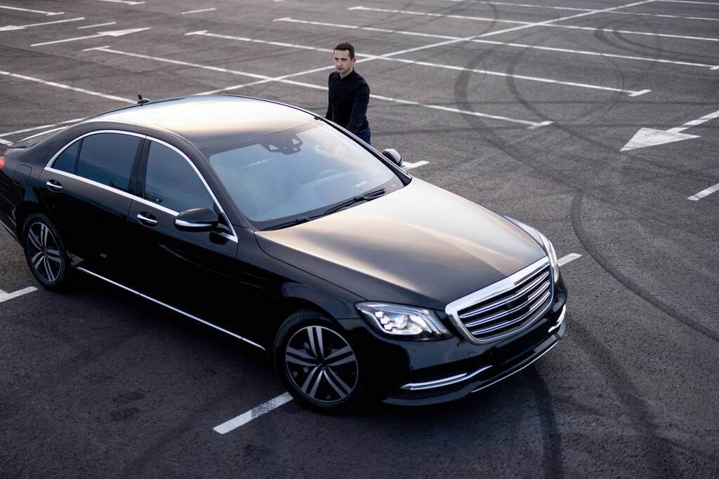 Chauffeur near luxury car of business class on parking lot, view from above