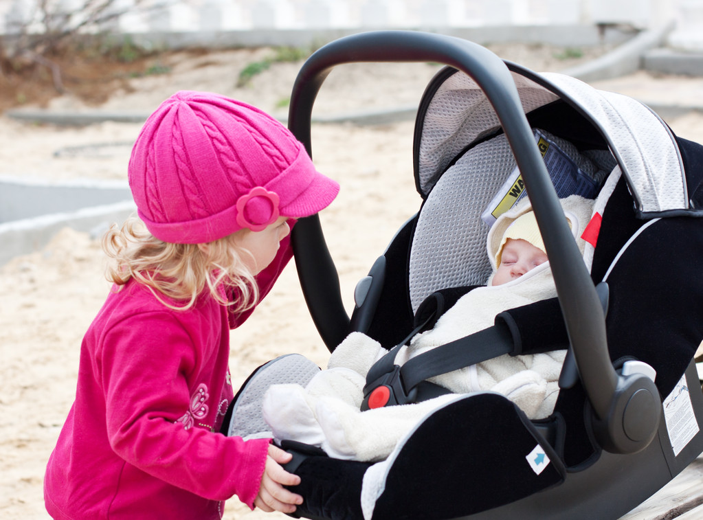 curious little girl looks in a car seat where sleeping brother