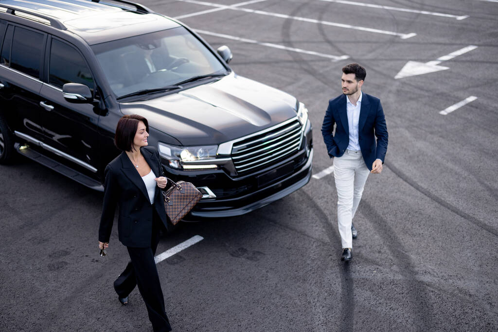 Business couple walking on parking lot, arrived by luxury SUV taxi, view from above. Concept of transportation and business trips
