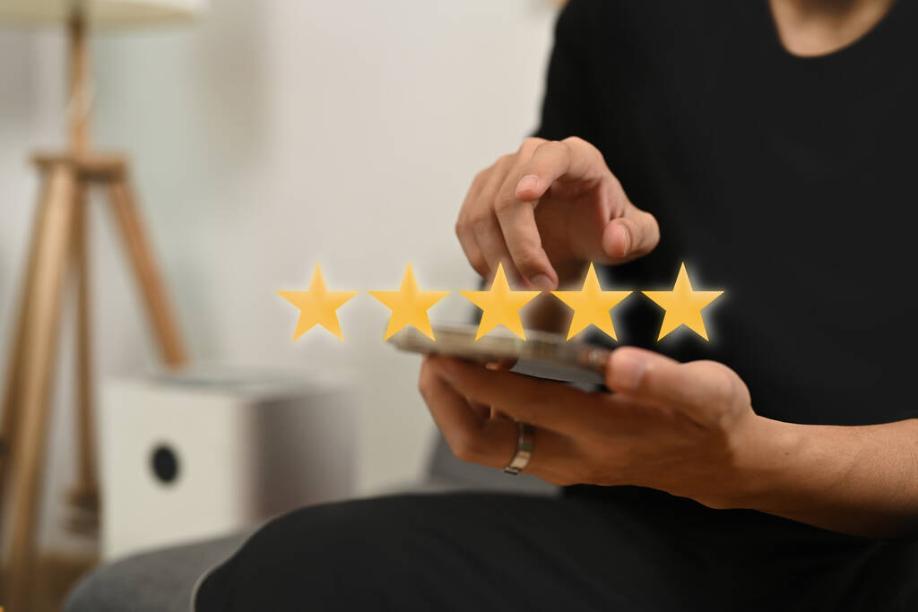 Young man pressing on smartphone screen giving positive feedback with gold five star rating.