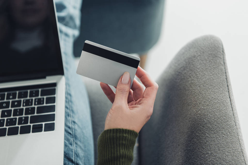 Cropped view of woman holding credit card near laptop
