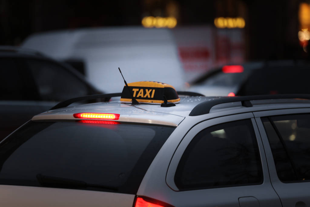 Taxi car with yellow checkered sign on city street in evening, closeup