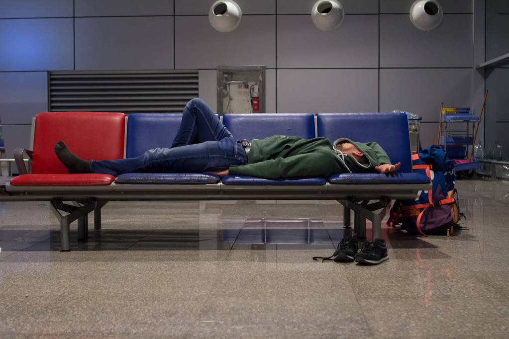 young tourist man with a backpack sleeping on chairs in the airport in anticipation of the aircraft due to flight delays