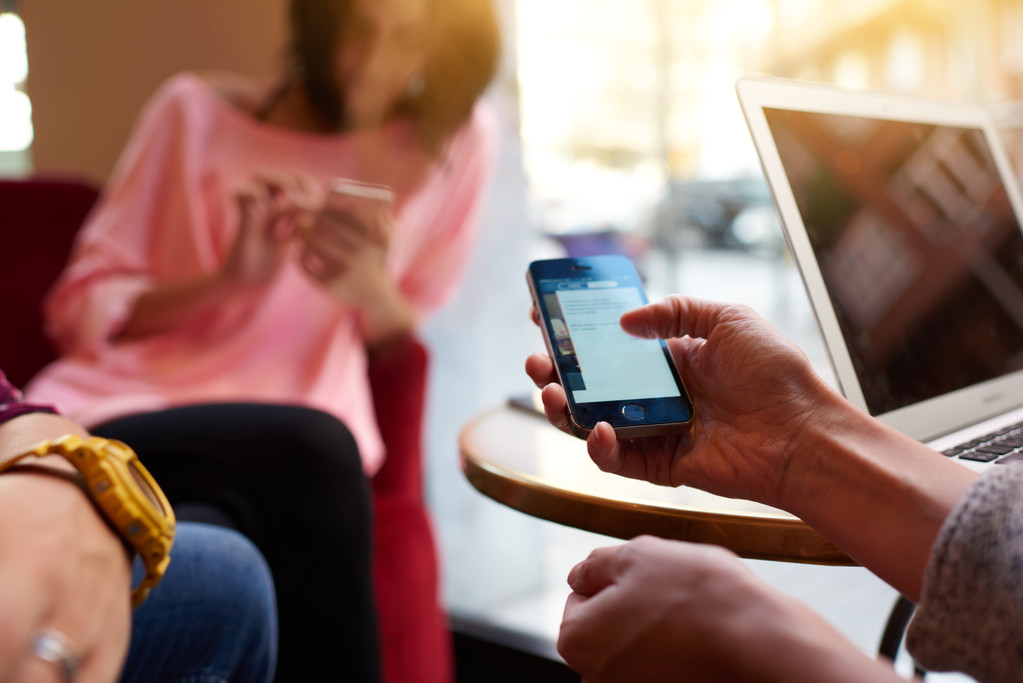 Closeup of woman is checking e-mail on her cell phone, while is resting after work on portable laptop computer. Closely of young person is using mobile phone for search information during rest in cafe