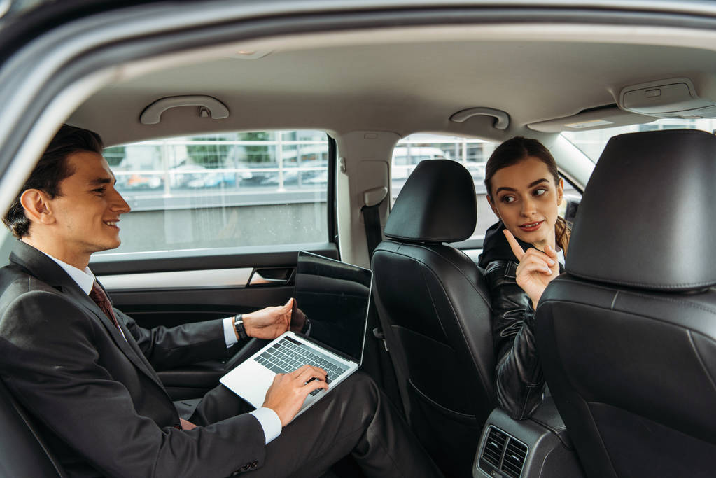 Driver talking with businessman sitting in taxi with laptop