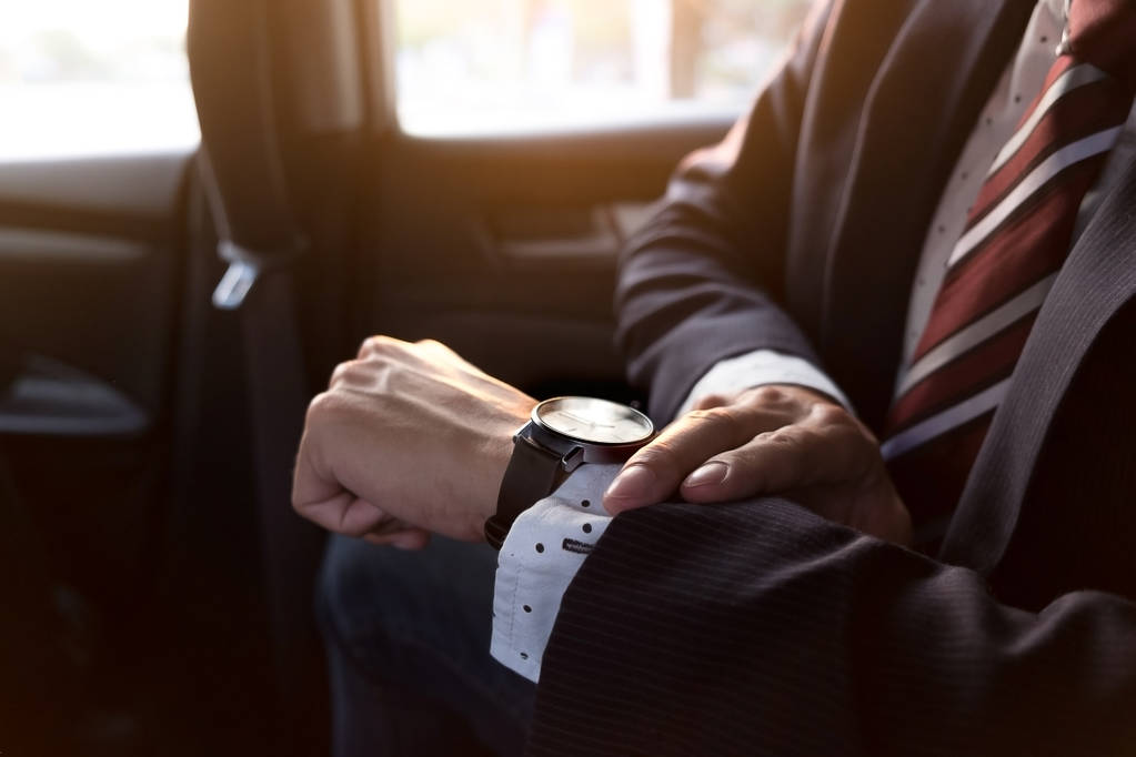 Handsome businessman looking on wrist watch in car