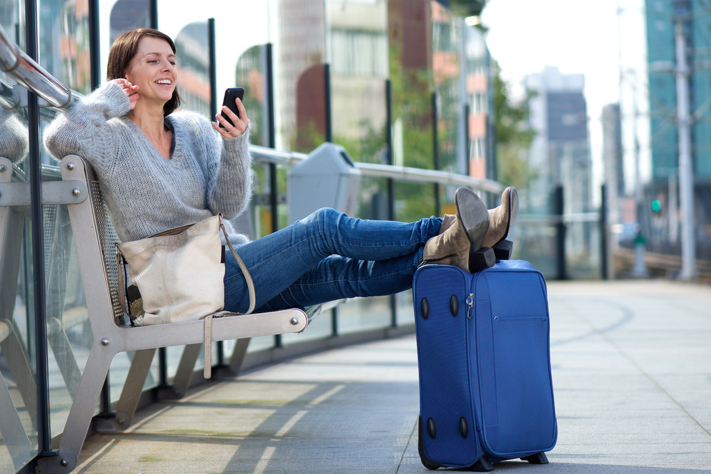 Portrait of an older travel woman relaxing with bag and smiling at mobile phone