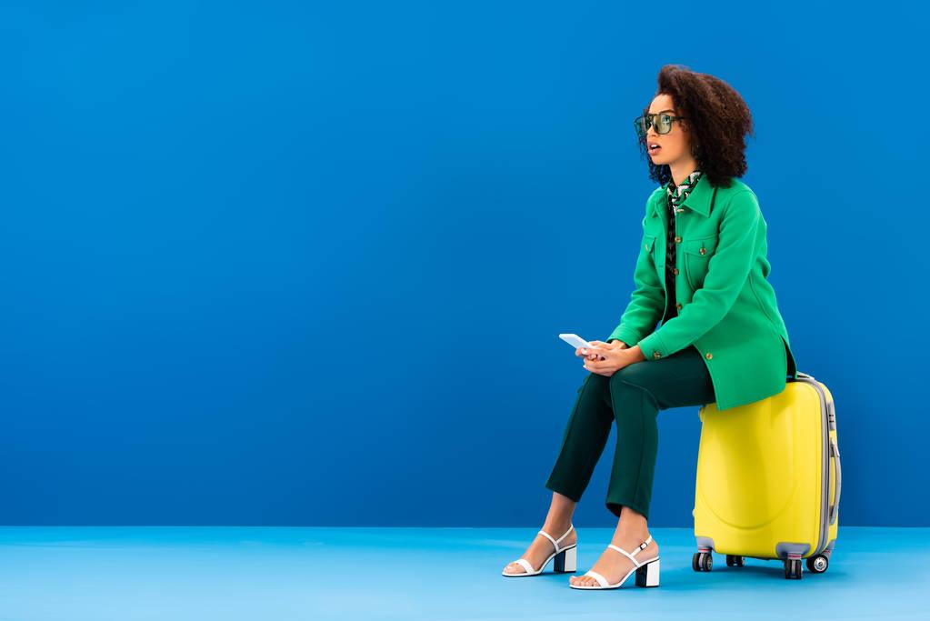 Woman sitting on travel bag holding the smartphone